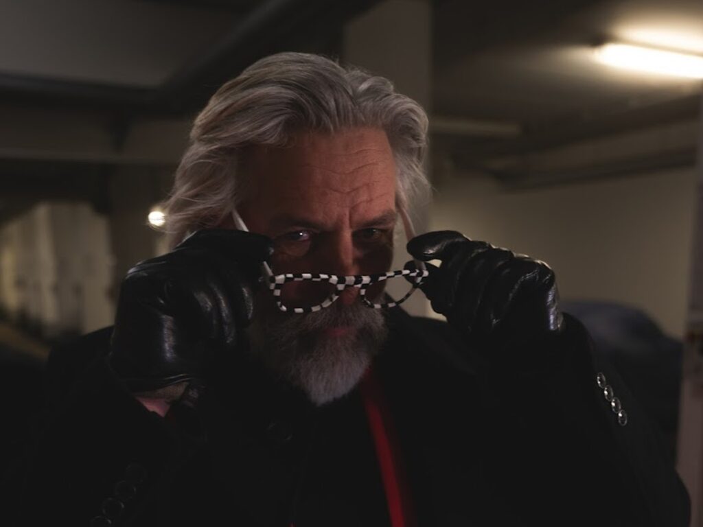 in Mann mit grauem Haar und Bart trägt schwarze Lederhandschuhe und setzt sich in einem dunklen Raum eine auffällige Nachtfahrbrille mit Schachbrettmuster auf. Die Brille ist speziell zur Reduzierung von Blendungen und für bessere Sicht bei Dunkelheit entwickelt.